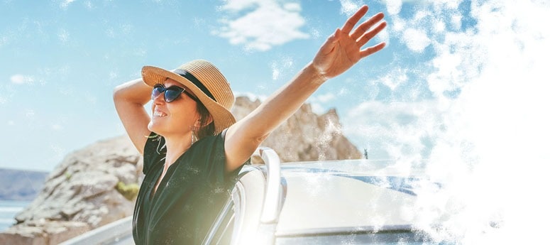 una mujer con sombrero y gafas de sol se sienta en la parte trasera de un coche con los brazos extendidos .