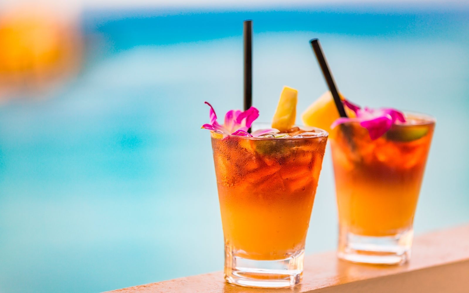 two cocktails with straws and flowers on them are sitting next to a pool .