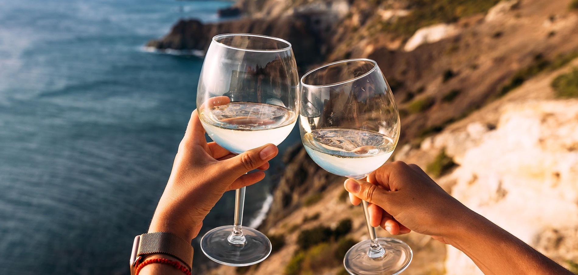 dos personas sostienen dos copas de vino frente al océano