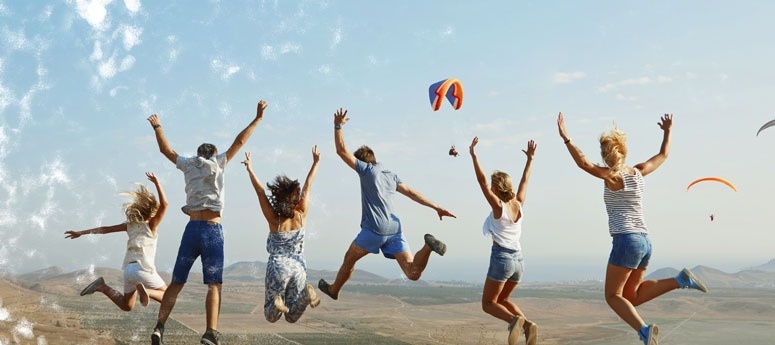 a group of people jumping in the air with a parachute in the background