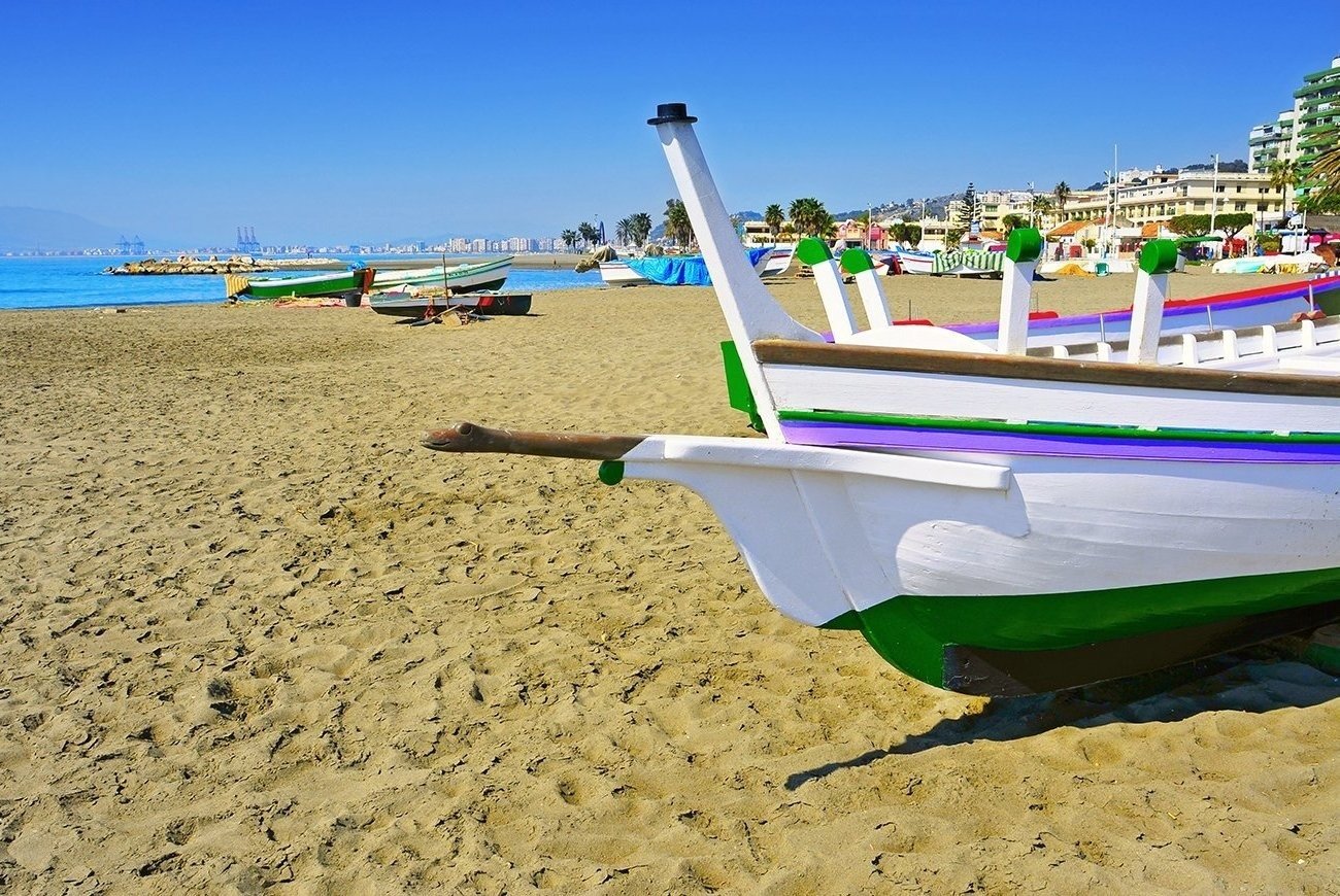 a green and white boat sits on a sandy beach