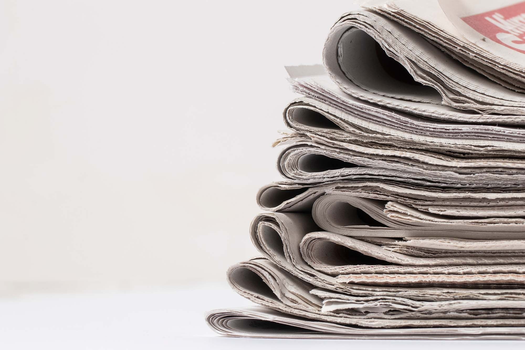 Una estantería muestra numerosos periódicos, la mayoría alemanes, con sus titulares visibles en un expositor de alambre.