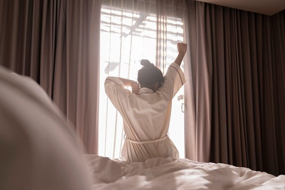 una mulher estira os braços en frente a uma janela
