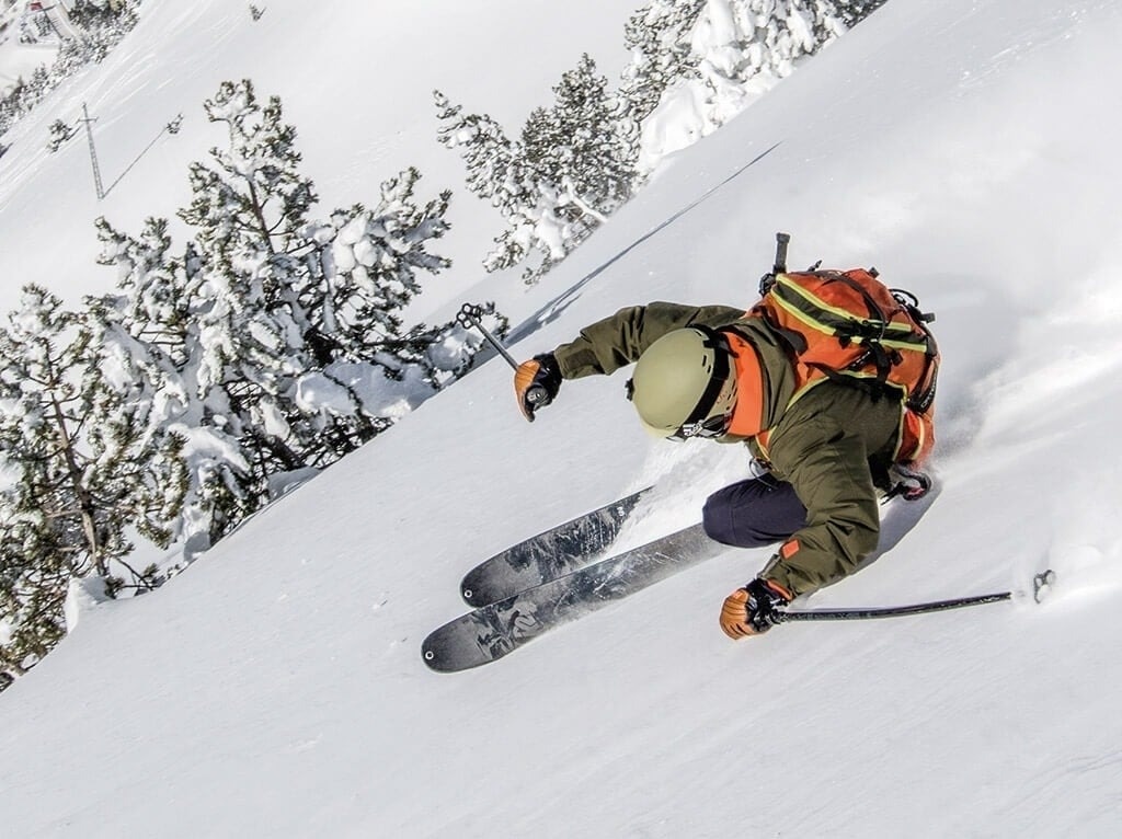 un esquiador con un casco y una mochila baja por una ladera cubierta de nieve