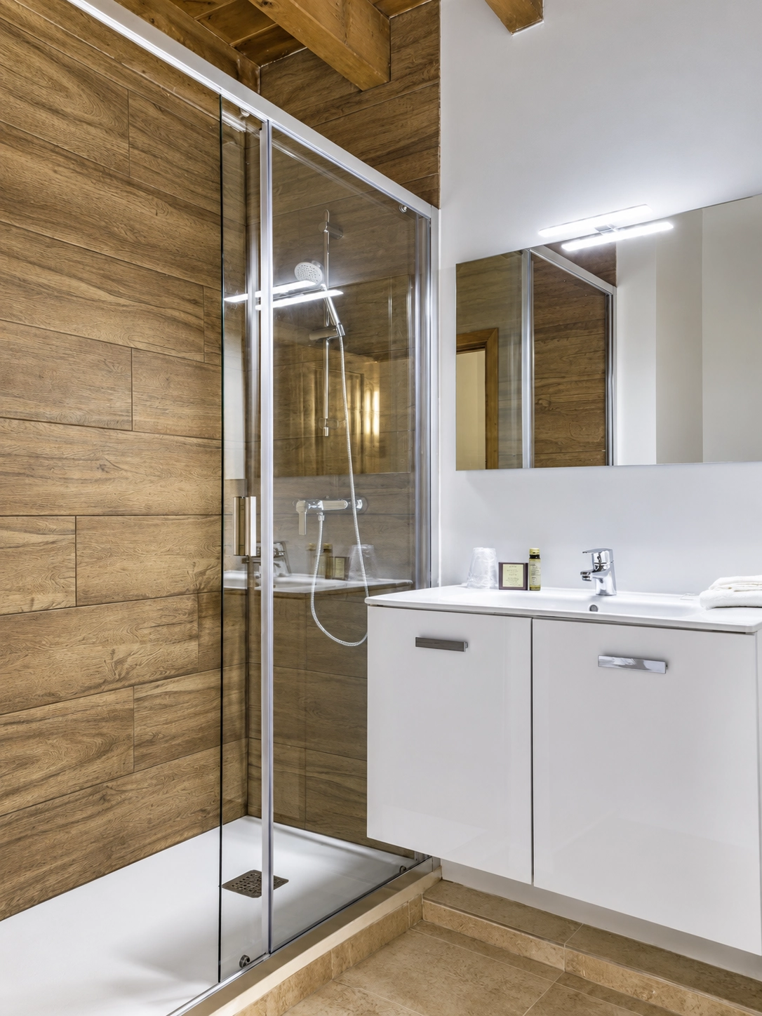 Baño moderno con ducha de cristal, lavabo blanco y pared de madera. SNÖ Vall de Boi