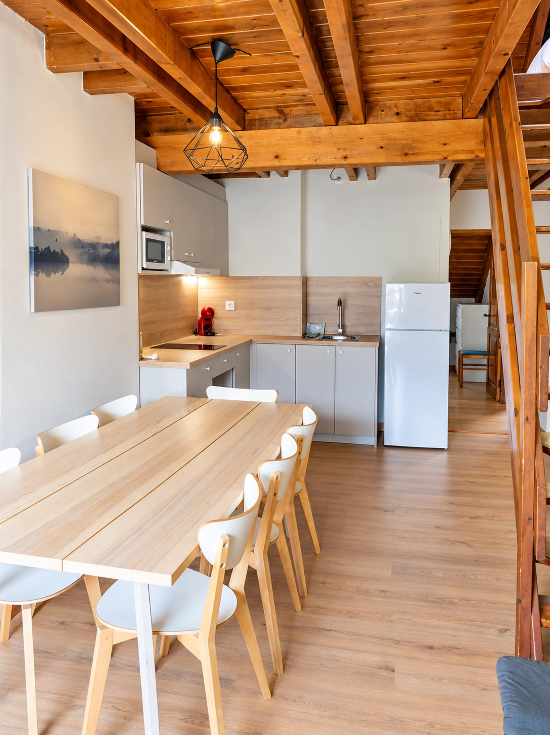 Cocina y comedor abiertos con mesa de madera y sillas blancas. SNÖ Vall de Boi.