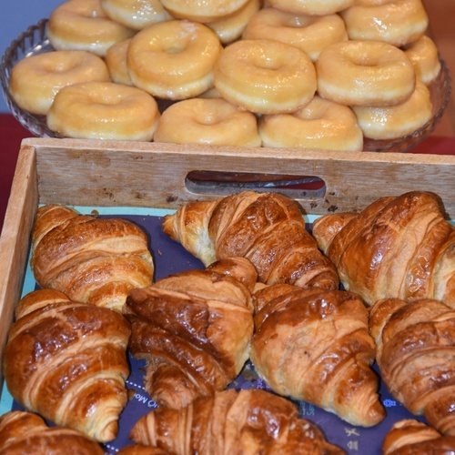 a tray of croissants sits next to a tray of glazed donuts