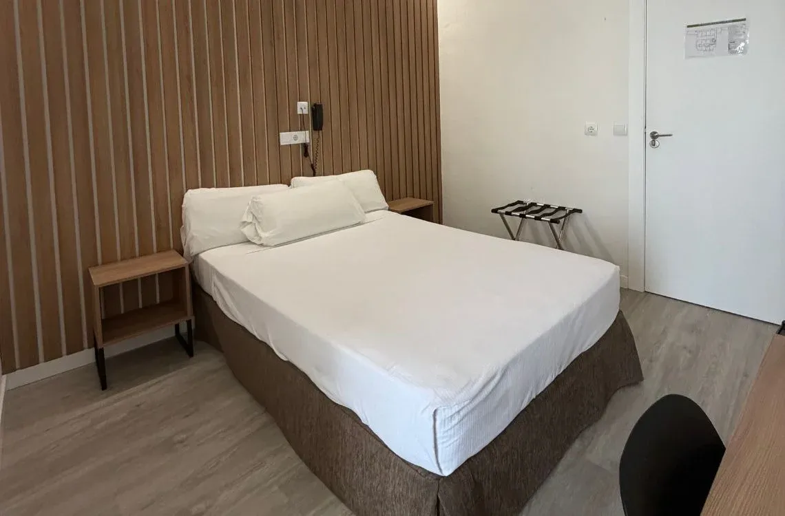 Cama cómoda en habitación de hotel moderna con pared de madera y mesita de noche, ideal para tu Hotel Victoria Centro.