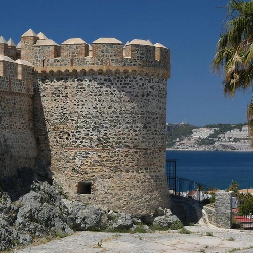 Vista de castillo histórico con palmeras y mar, sitio perfecto para Hotel Victoria Centro.