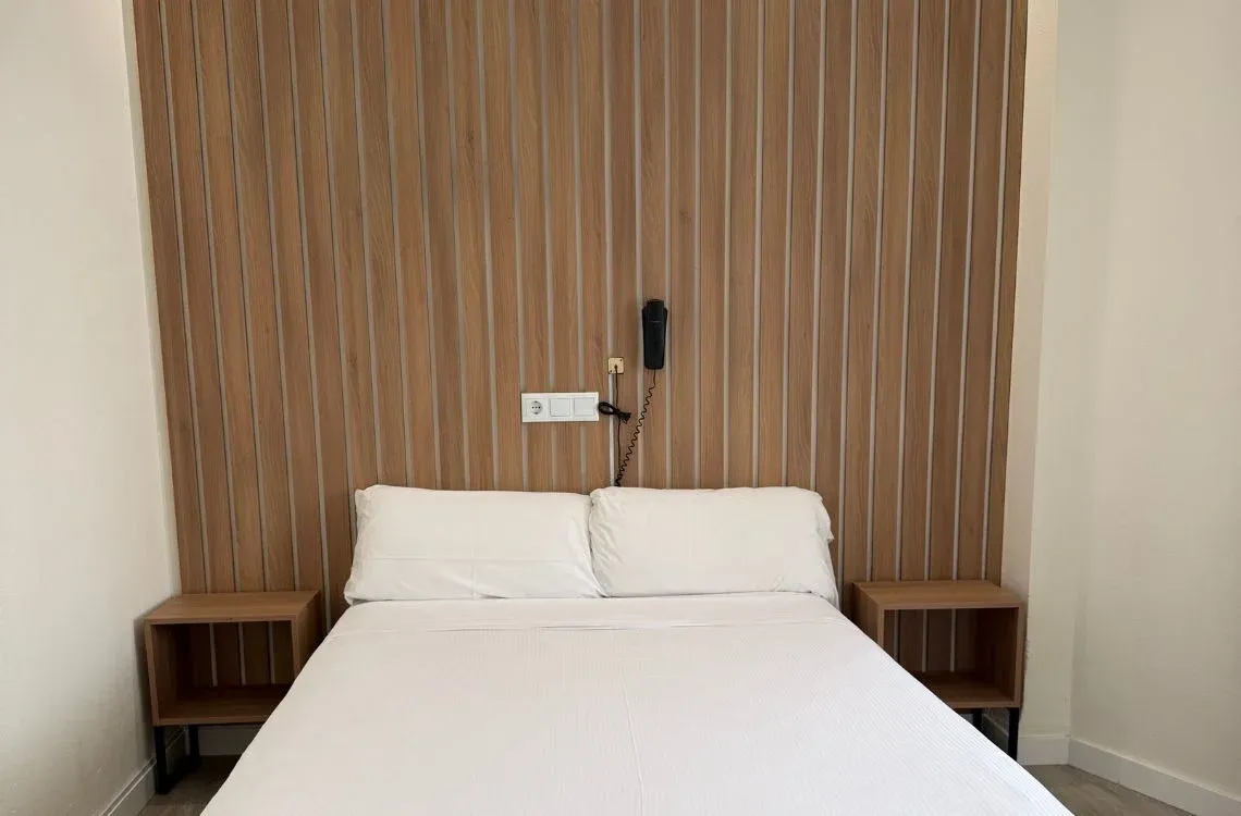 Cama doble con mesitas de noche y cabecero de madera en habitación de hotel. Hotel Victoria Centro