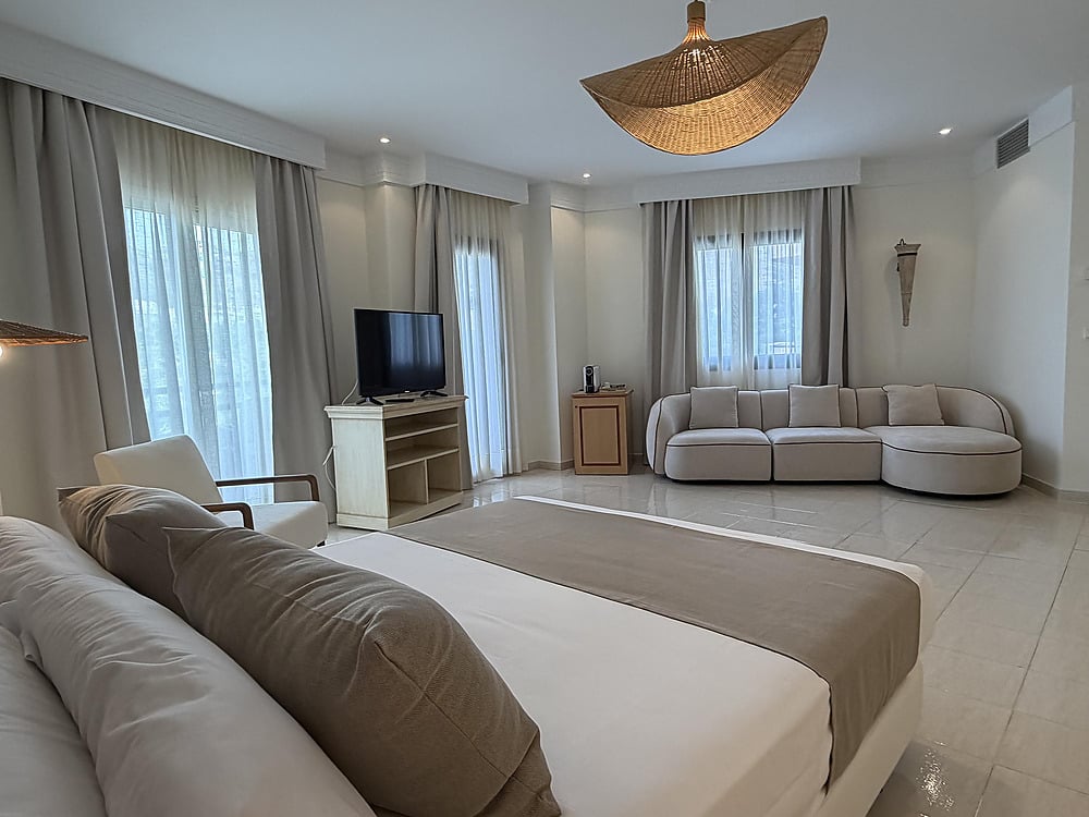 Victoria Playa spacious suite with king bed, red sofa, and balcony.