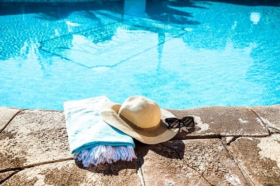 una toalla sombrero y gafas de sol junto a una piscina