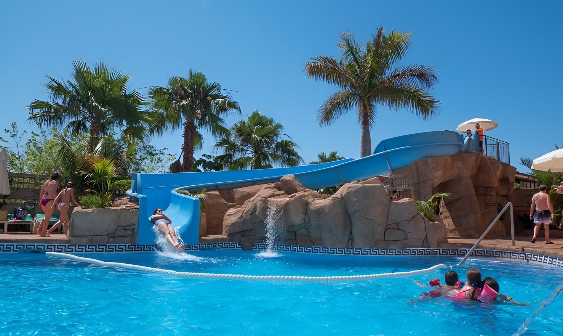 un tobogán azul en una piscina con palmeras en el fondo