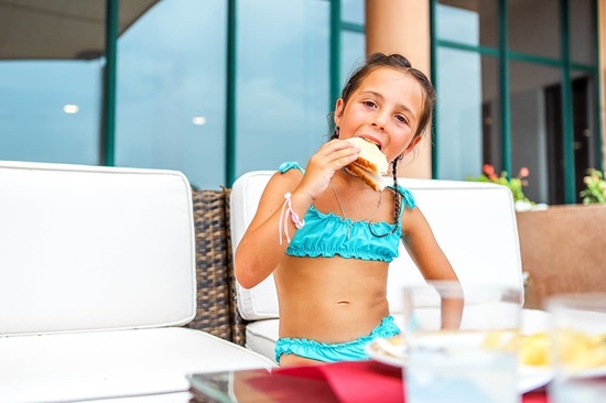 una niña en bikini azul está comiendo una hamburguesa