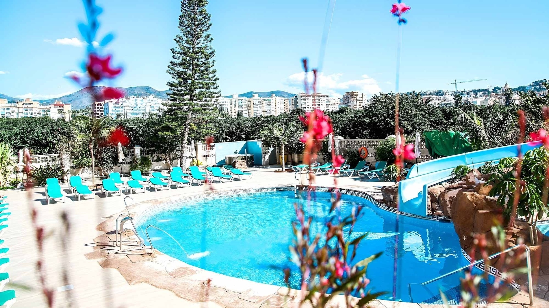 una piscina rodeada de sillas y flores con un tobogán en el fondo