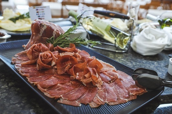 a plate of meat with tongs and a bottle of wine in the background