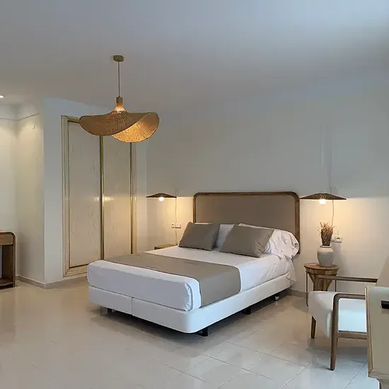 Habitación de hotel Victoria Playa: cama doble, sillón a rayas y espejo dorado.