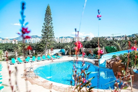 una piscina rodeada de sillas y flores con un tobogán en el fondo