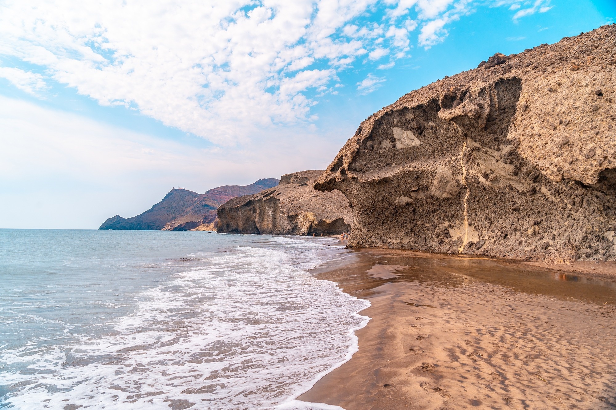 
                                    waves crashing on a sandy beach with mountains in the background