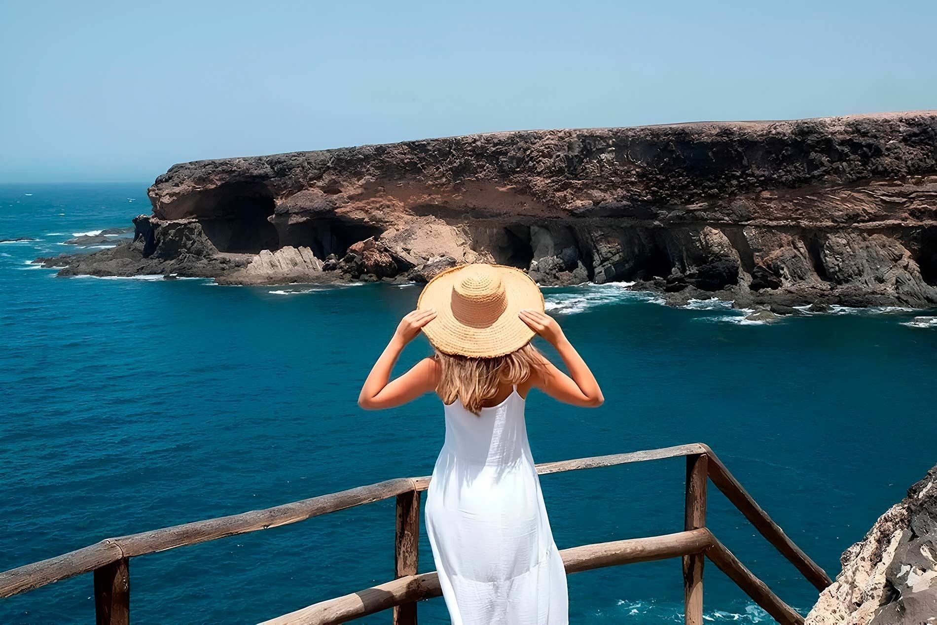 a woman in a white dress and straw hat looks out over the ocean