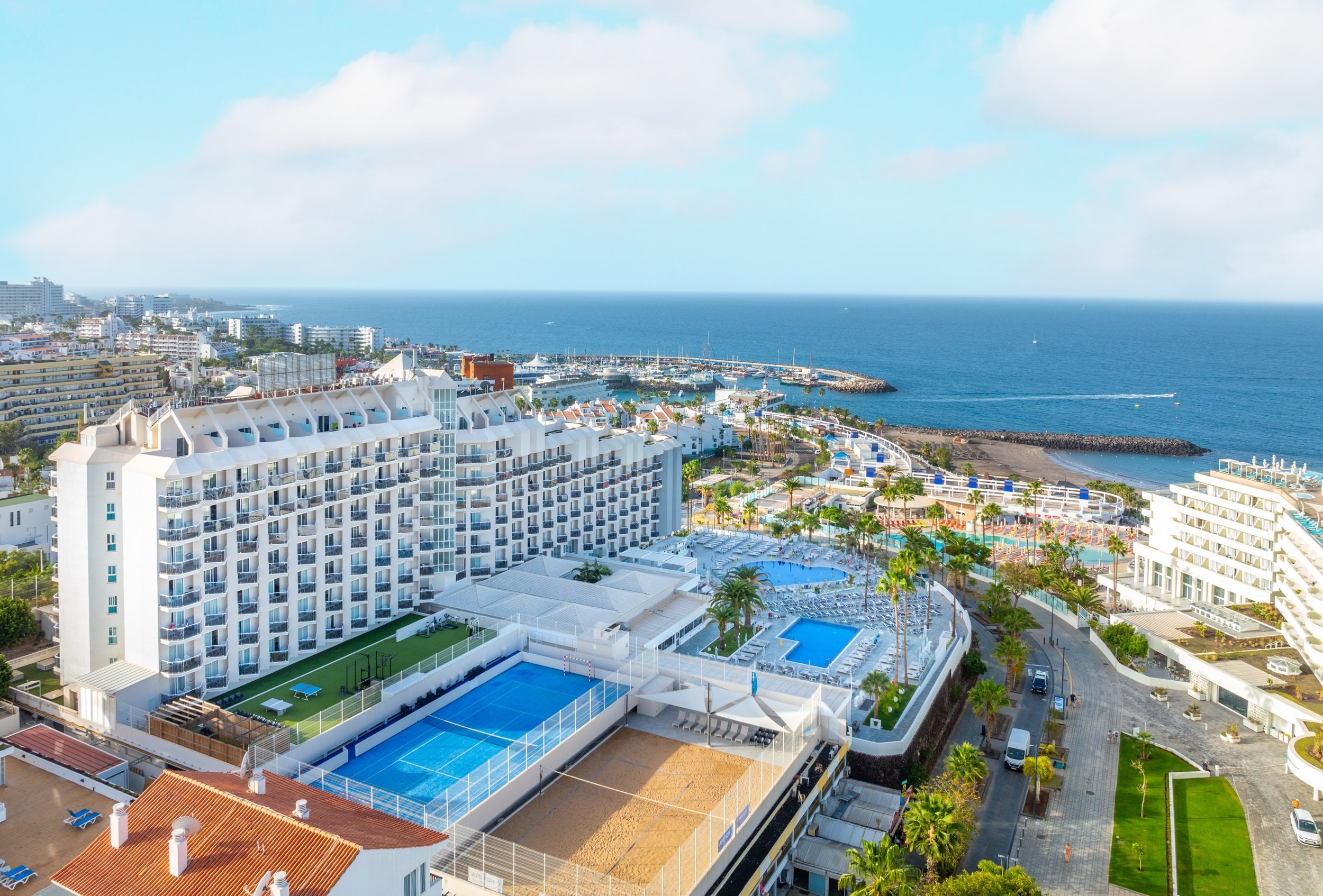 een groot witte hotel met een tennisbaan en een zwembad
