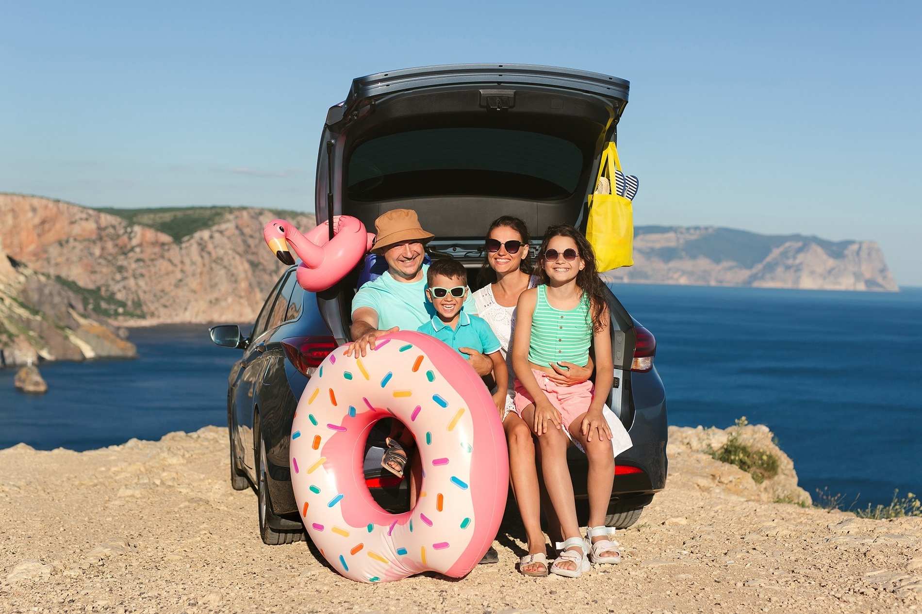 семья сидит в багажнике автомобиля с надувным пончиком и фламинго