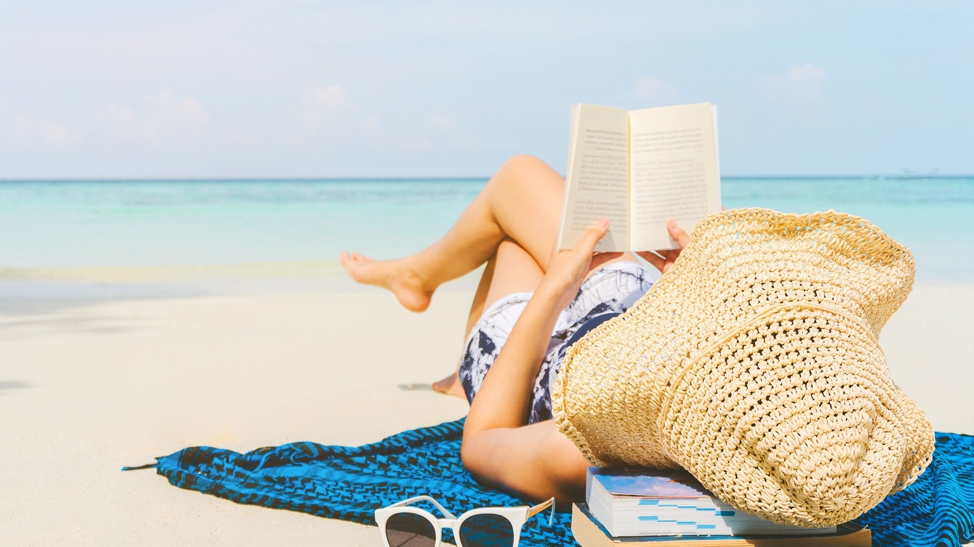 Een vrouw op het strand die een boek leest.