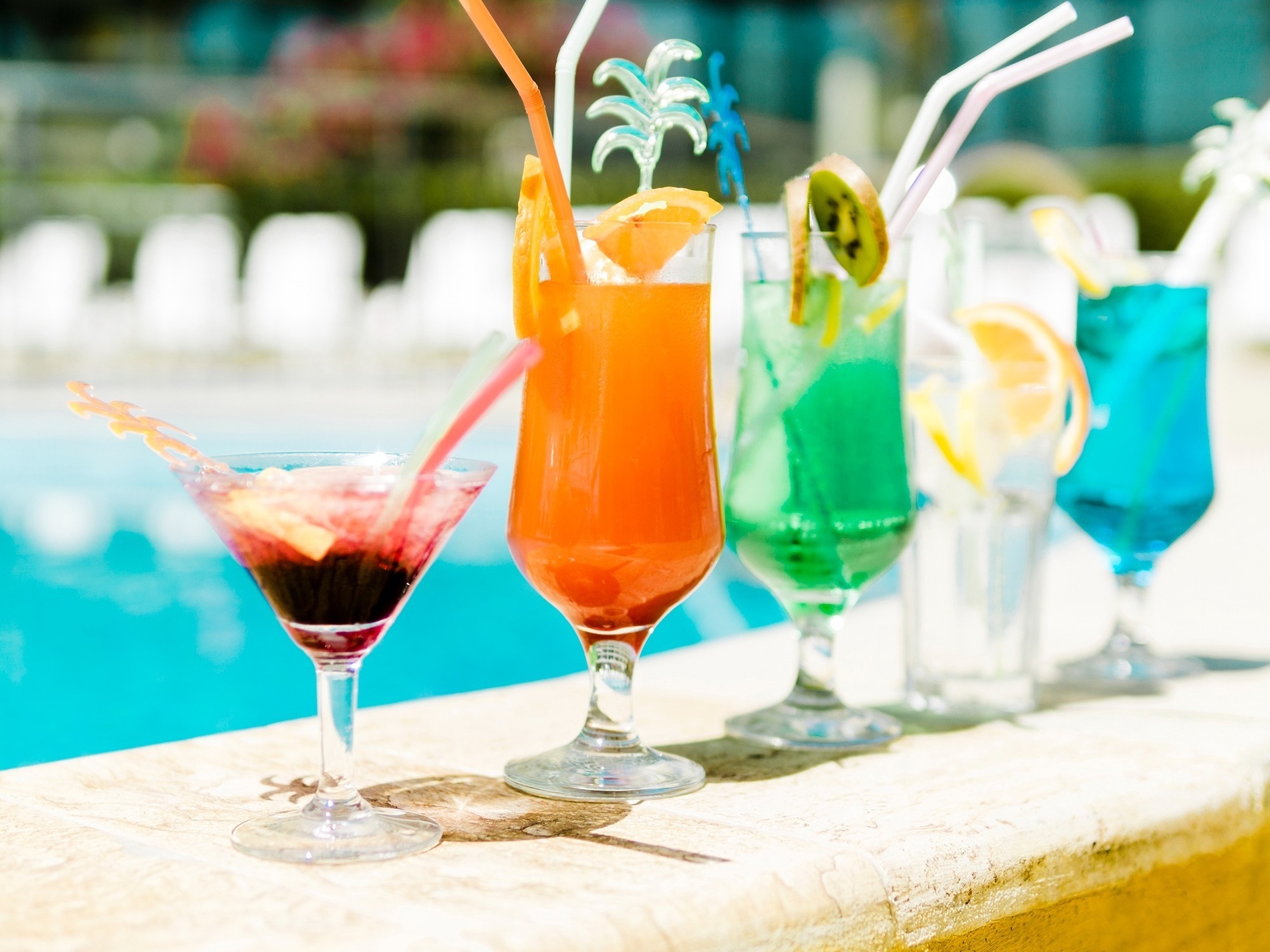 verschiedene Cocktails mit Strohhalmen neben einem Pool