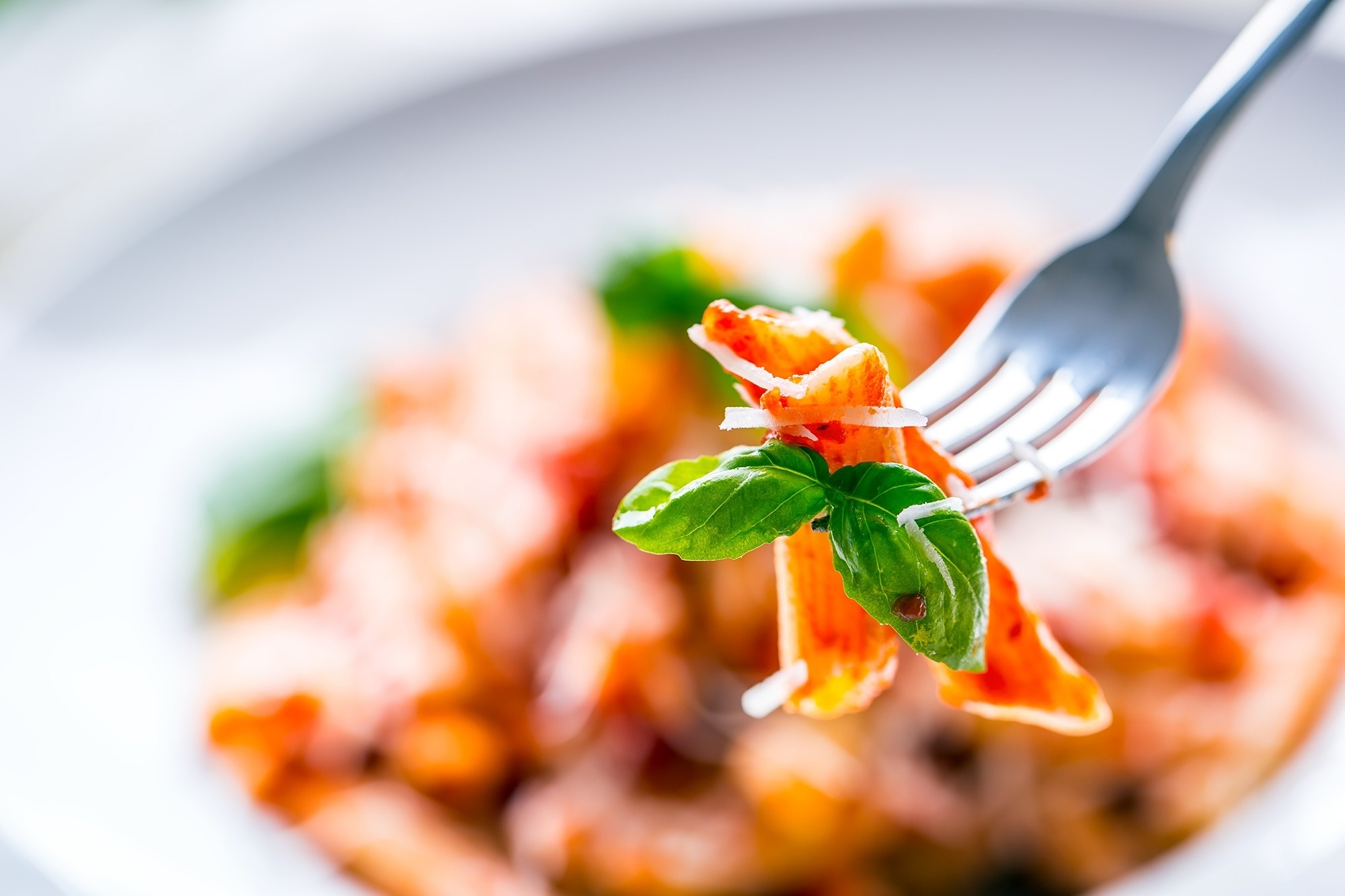 eine gabel hält einen stück pasta mit basilikum und parmesan