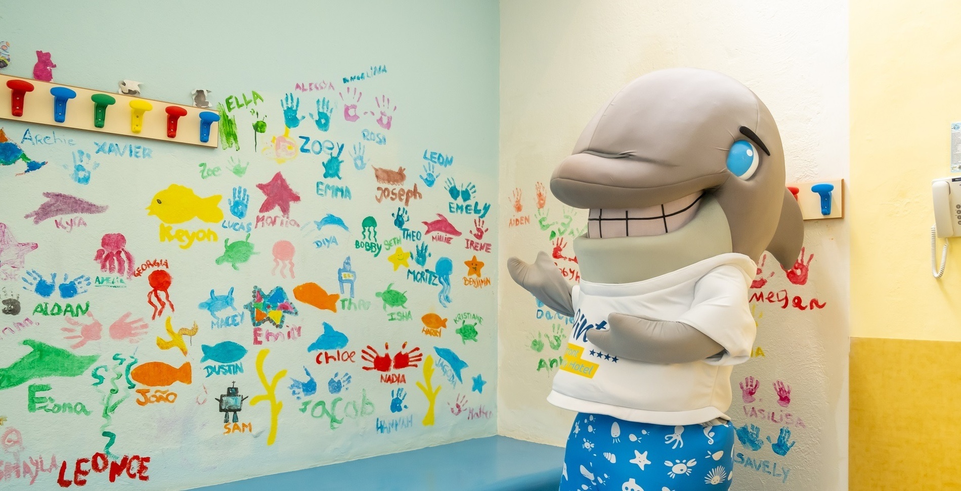 ein delfin maskottchen steht vor einer wand mit handabdrücken von kindern darauf