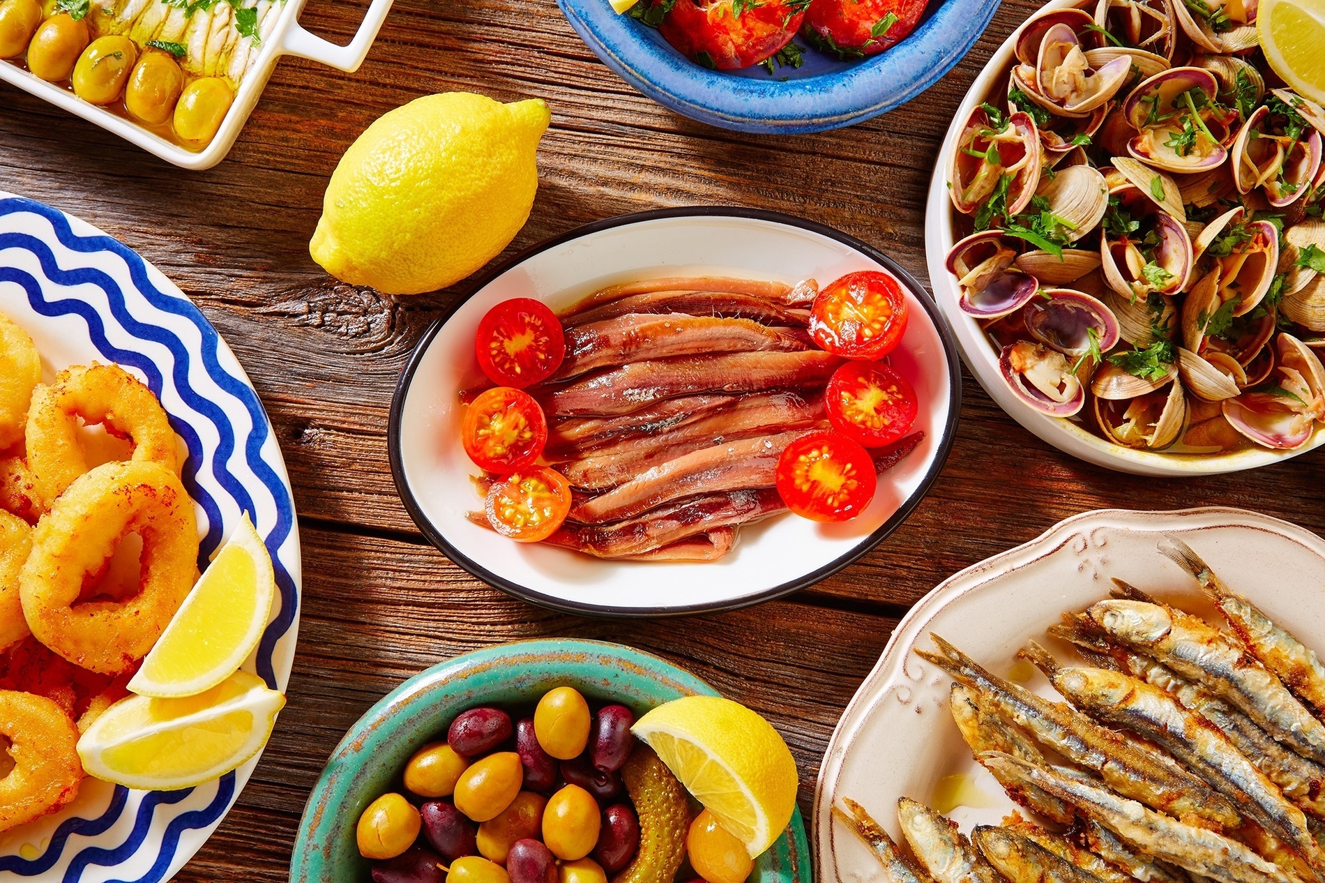 a wooden table topped with plates of food including anchovies tomatoes olives and lemons