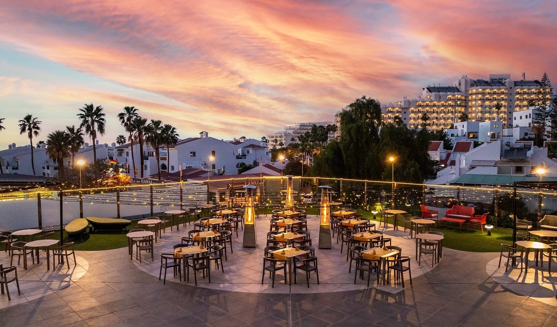 a row of tables and chairs on a rooftop with a hotel in the background