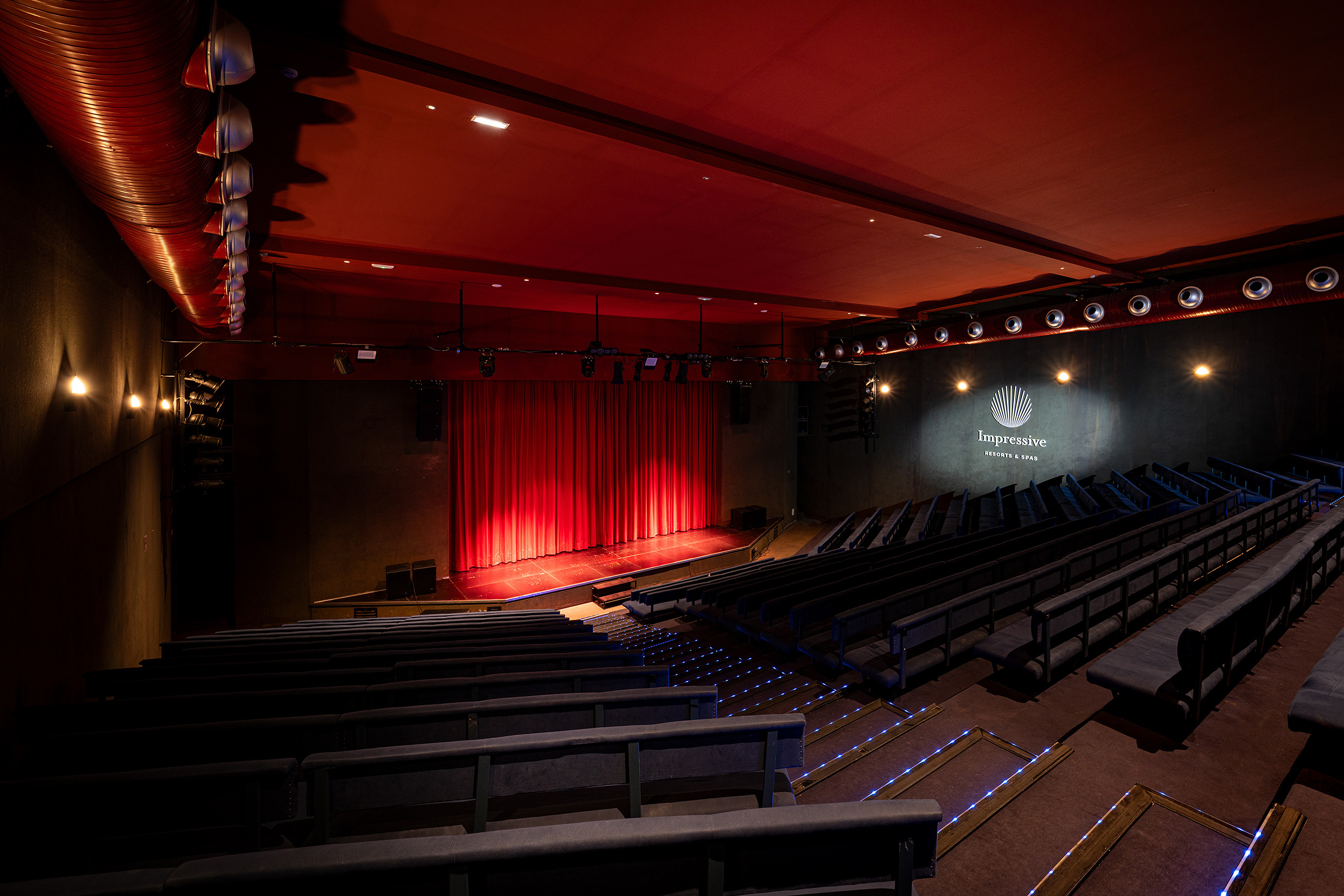 Auditorio de teatro con cortinas rojas y asientos azules. Impressive Playa Granada