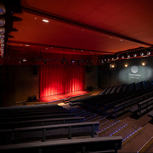 Auditorio con butacas azules, cortinaje rojo y foco de escenario. Impressive Playa Granada