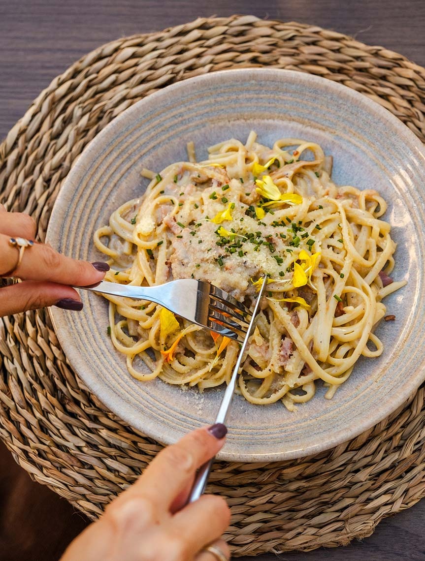 Leckere Pasta mit essbaren Blüten, serviert auf einem Teller auf einer Weidenmatte Impressive Playa Granada