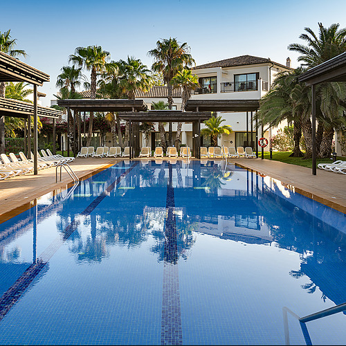 Piscina de hotel con palmeras y tumbonas bajo un cielo azul claro. Impressive Playa Granada