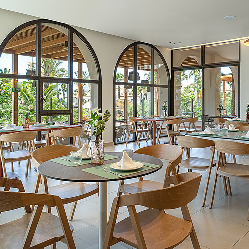 Comedor de hotel moderno con mesas de madera y vistas al exterior, ideal para Impressive Playa Granada.