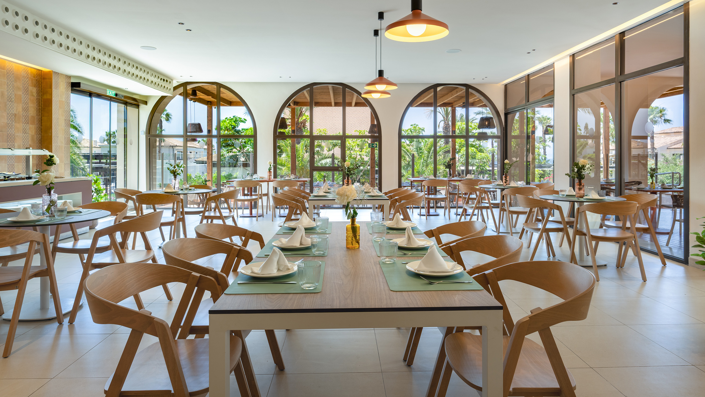 Comedor de hotel moderno con mesas de madera y sillas, amplios ventanales y luz natural. Impressive Playa Granada