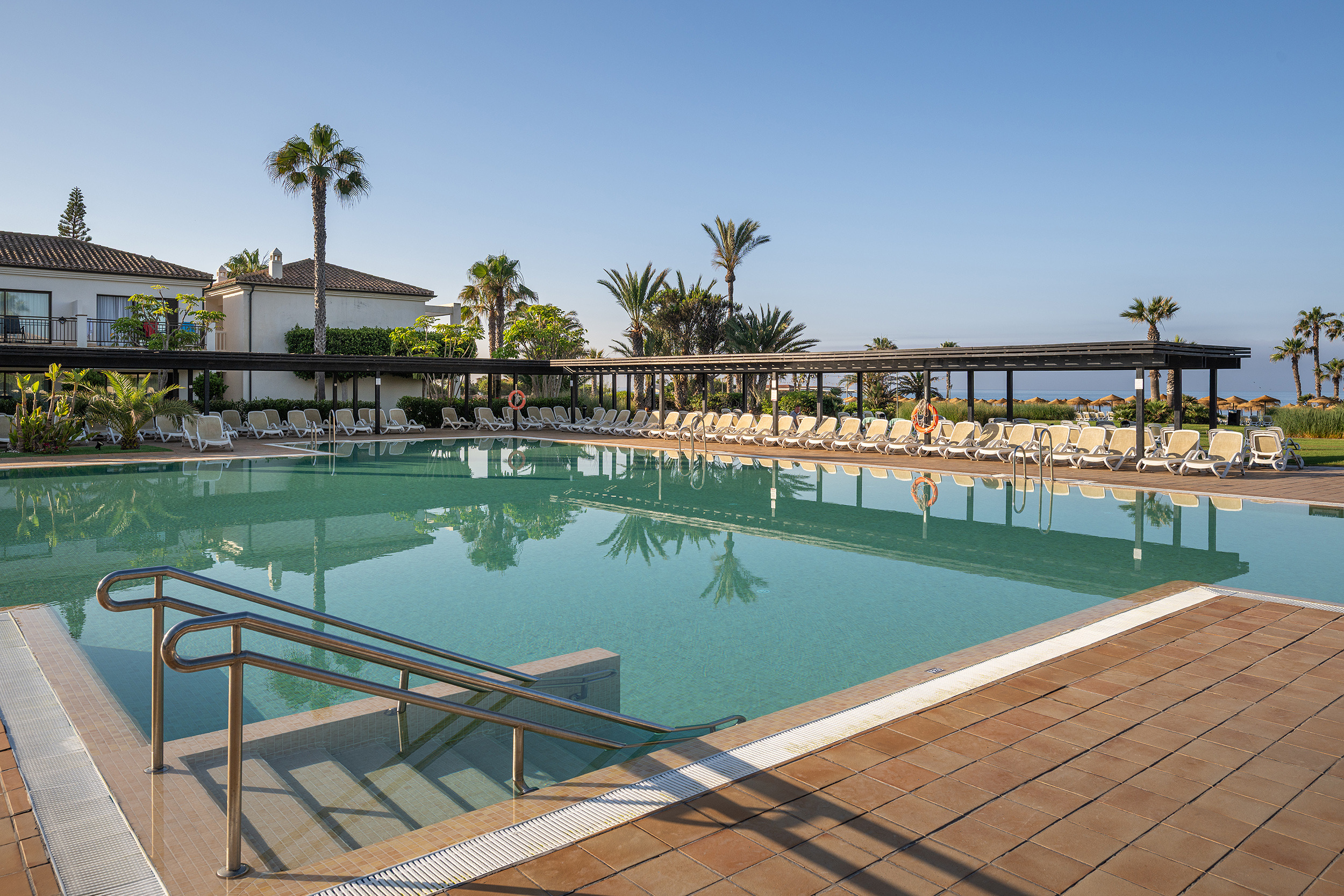 Piscina hotelera con palmeras y tumbonas para relajarse Impressive Playa Granada.