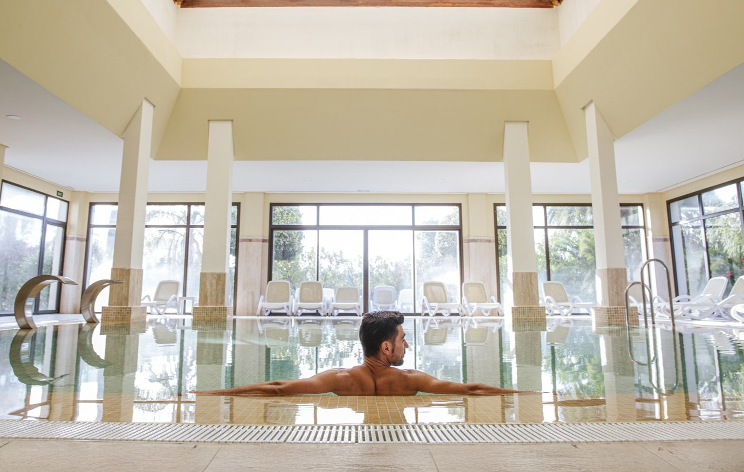 Hombre relajado en piscina interior, spa del hotel con Impressive Playa Granada.