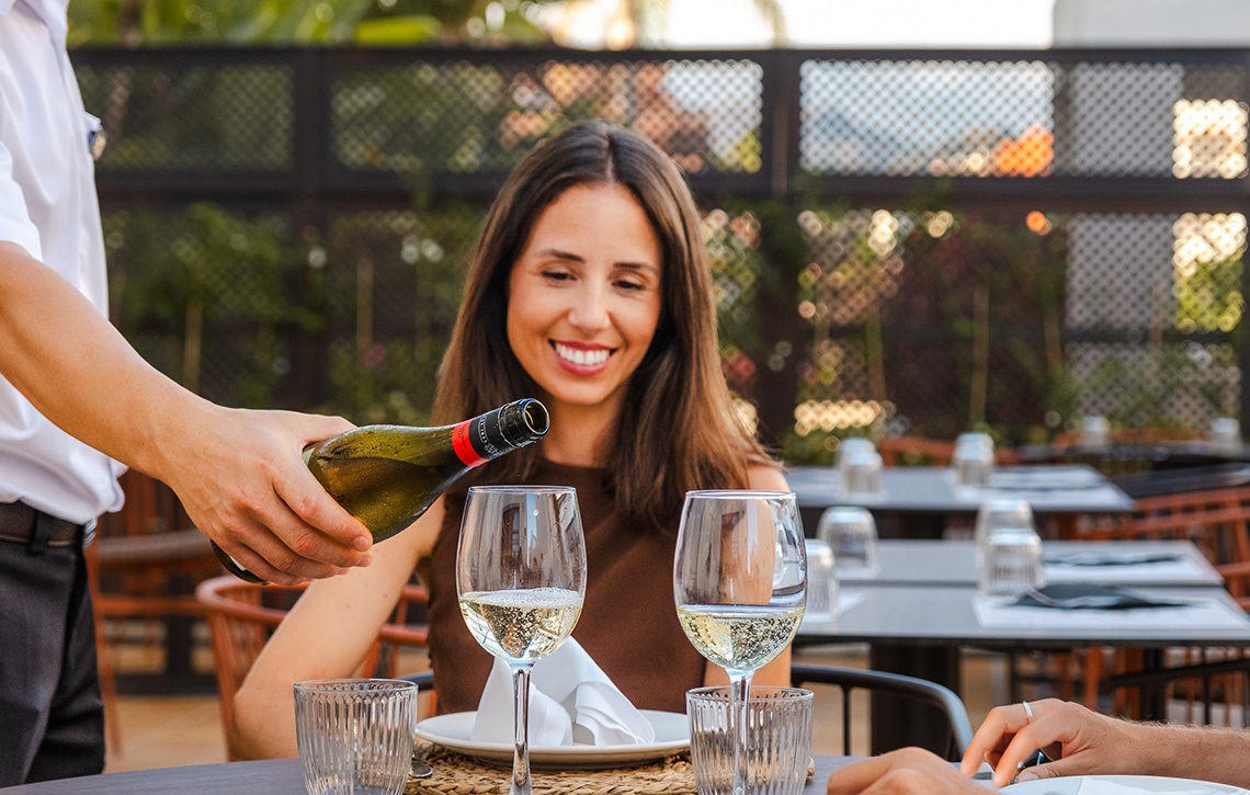 Romantisches Abendessen: Kellner schenkt Sekt für lächelnde Frau imImpressive Playa Granada