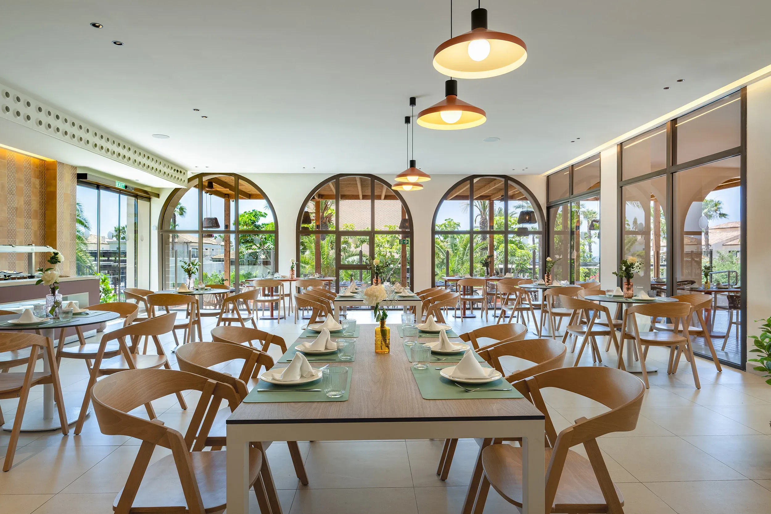 Comedor exterior con mesas y sillas de madera, decorado con plantas y lámparas de mimbre, ideal para Impressive Playa Granada.