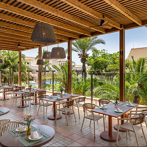 Restaurante de hotel moderno con mobiliario de madera, luces colgantes y área de buffet Impressive Playa Granada.