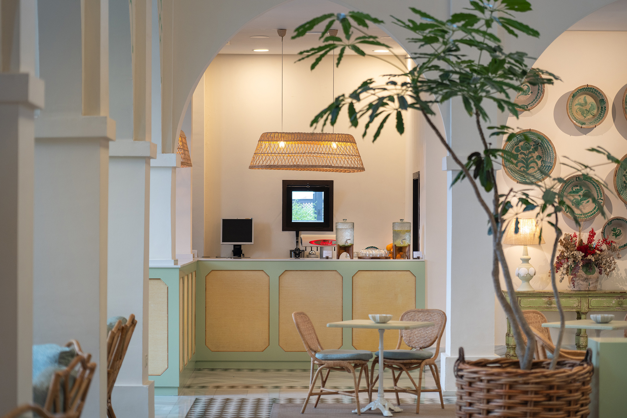Salón y bar de hotel con mesas de ratán, plantas exuberantes y decoración temática Impressive Playa Granada.