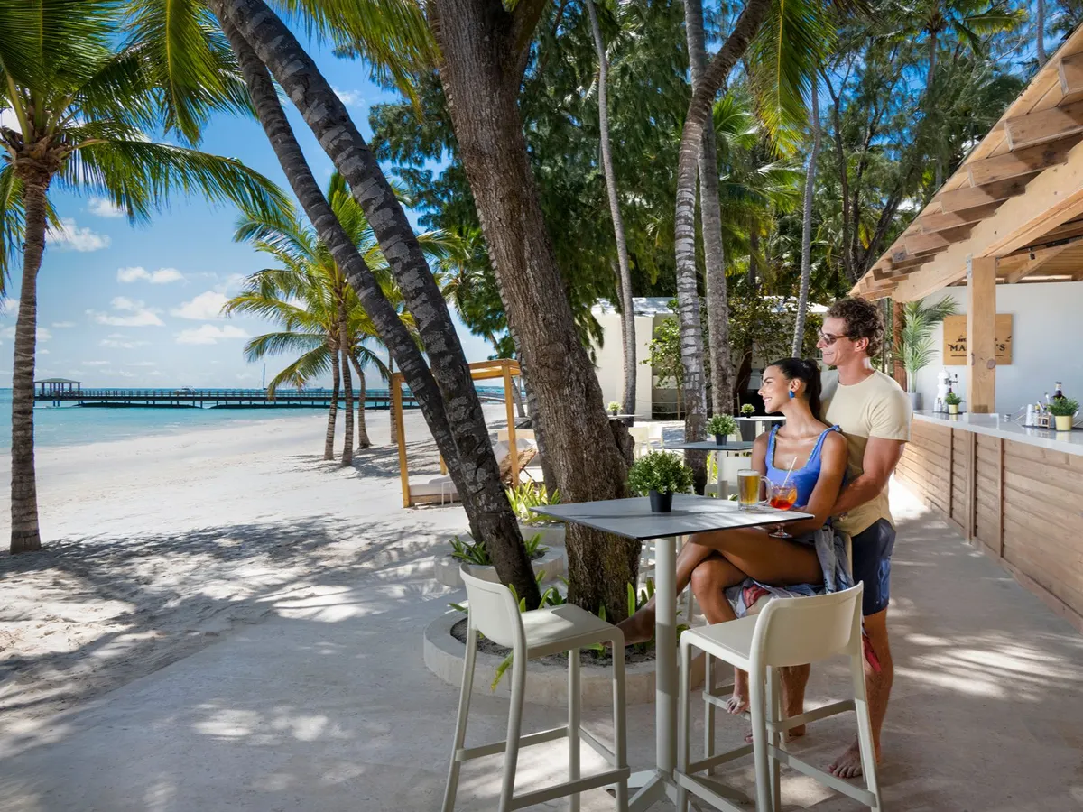 Pareja tomando una copa en un bar de playa rodeado de palmeras. Impressive Royal Punta Cana