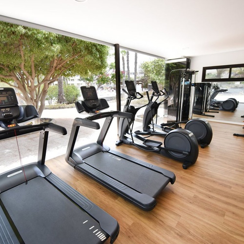 Modernes Fitnessstudio im Impressive Zocos Lanzarote mit Laufbändern, Crosstrainern und Blick ins Grüne.