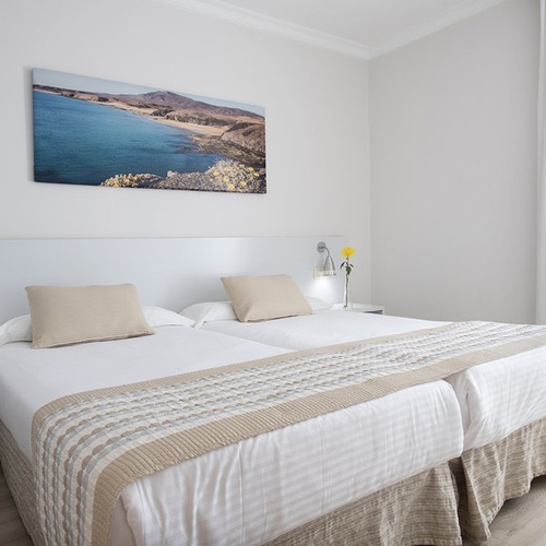 Helles, modernes Hotelzimmer im Impressive Zocos Lanzarote mit maritimer Kunst und bequemen Betten.