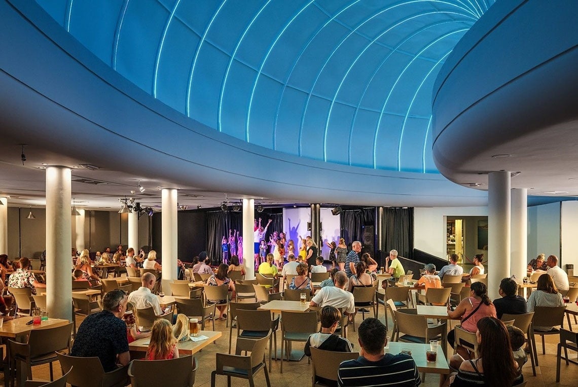 Gäste genießen Abendshow im modernen Hotel-Veranstaltungsraum mit Bühne und blauer Lichtdecke.