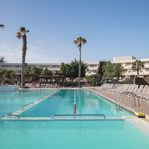 Impressive Zocos Lanzarote Hotel mit großem Außenpool, Palmen und Sonnenliegen unter blauem Himmel.