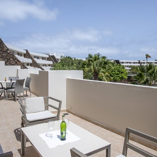 Geräumige Hotelterrasse mit Lounge- und Esstisch, Blick auf Grüne und die Gebäude des Impressive Zocos Lanzarote.